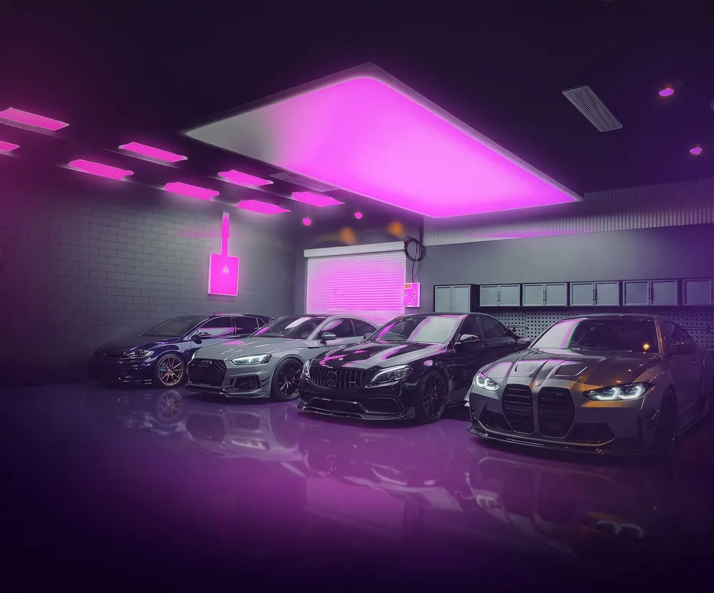 Four European performance cars parked under pink neon light in a garage
